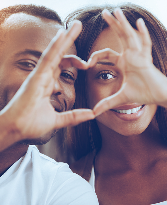 Photo of a smiling couple forming a heart with their hands.